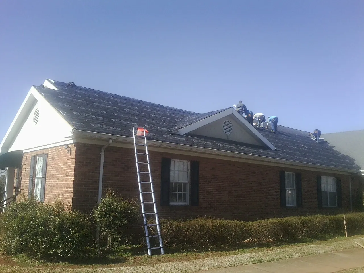 Crew tearing shingles off a brick ranch roof with a ladder set — Metal Roof Repair work by our crew in Powells Point