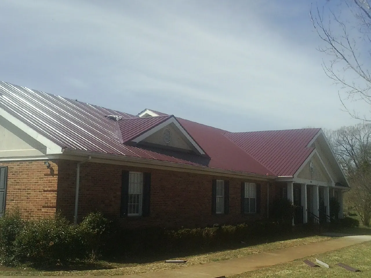 Red metal roof with gabled entries on a long brick building, from a Hail Damage Roof Repair job in Powells Point