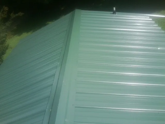 New green metal panels meeting at the ridge of a roof — Flat Roof Repair work by our crew in Powells Point