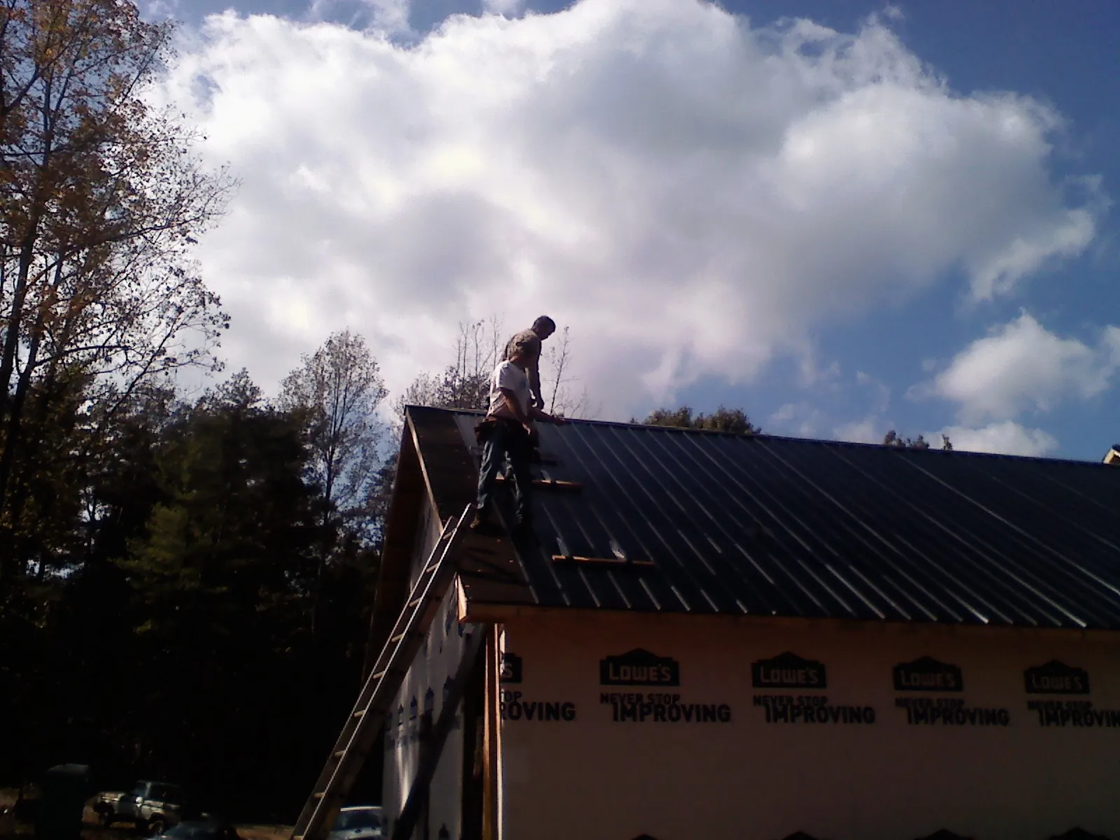Roofer fastening dark metal panels high against a cloudy sky, from a Roof Inspection job in Powells Point