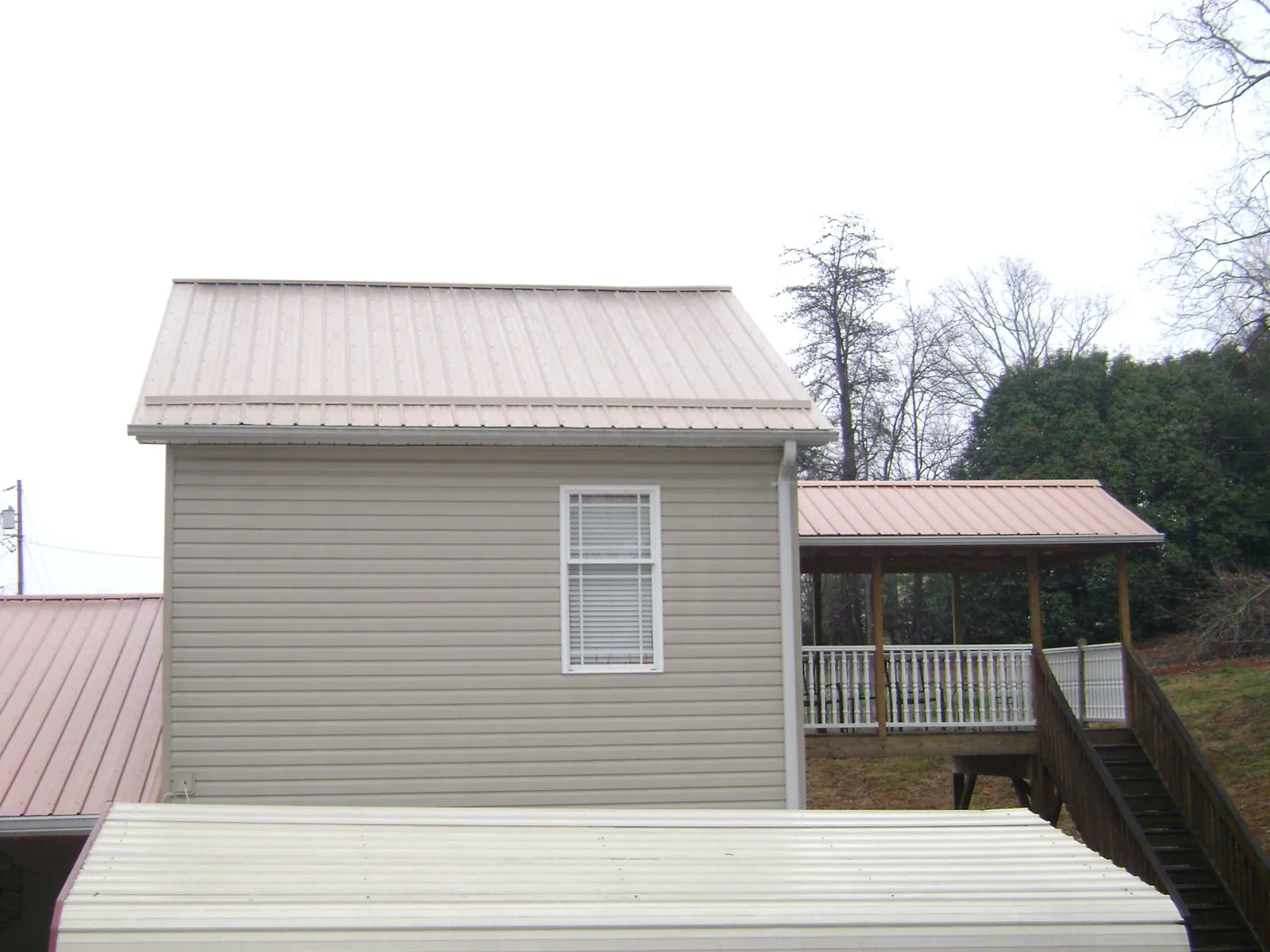 Tan metal roofs on a two story addition and attached porch, from a Roof Replacement job in Powells Point
